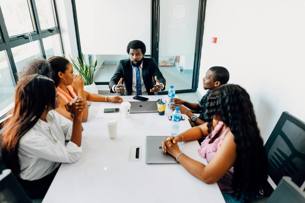 A group of people are sitting around a table in a meeting room. Find more afro-centric images at www.ninthgrid.com
